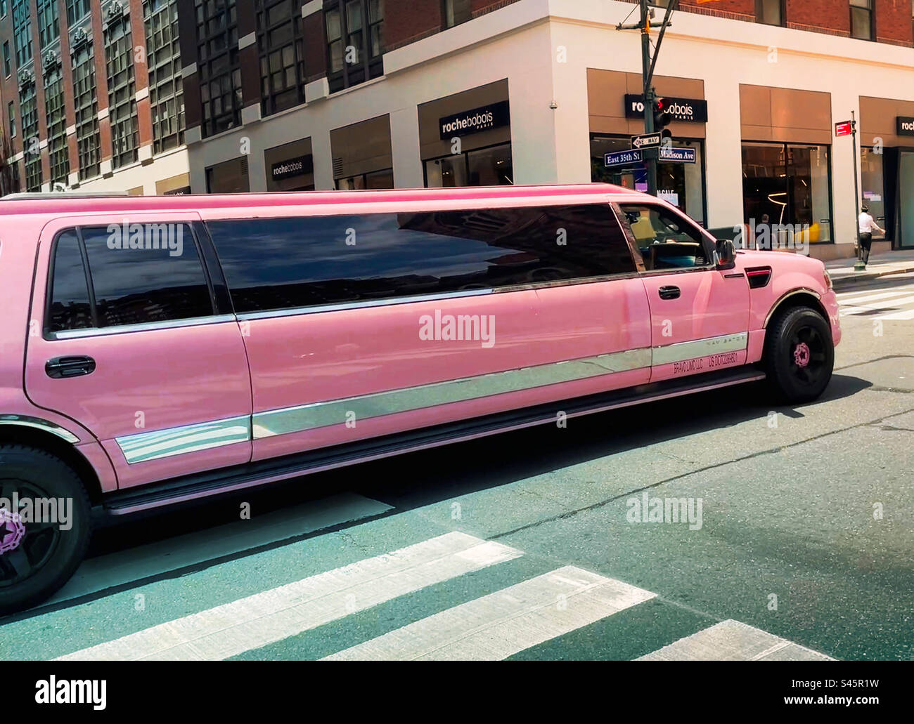 A vibrant pink stretch limousine cruises up Madison Avenue on a sunny summer day, 2023, New York City, United States - Smartphone Captured Stock Image