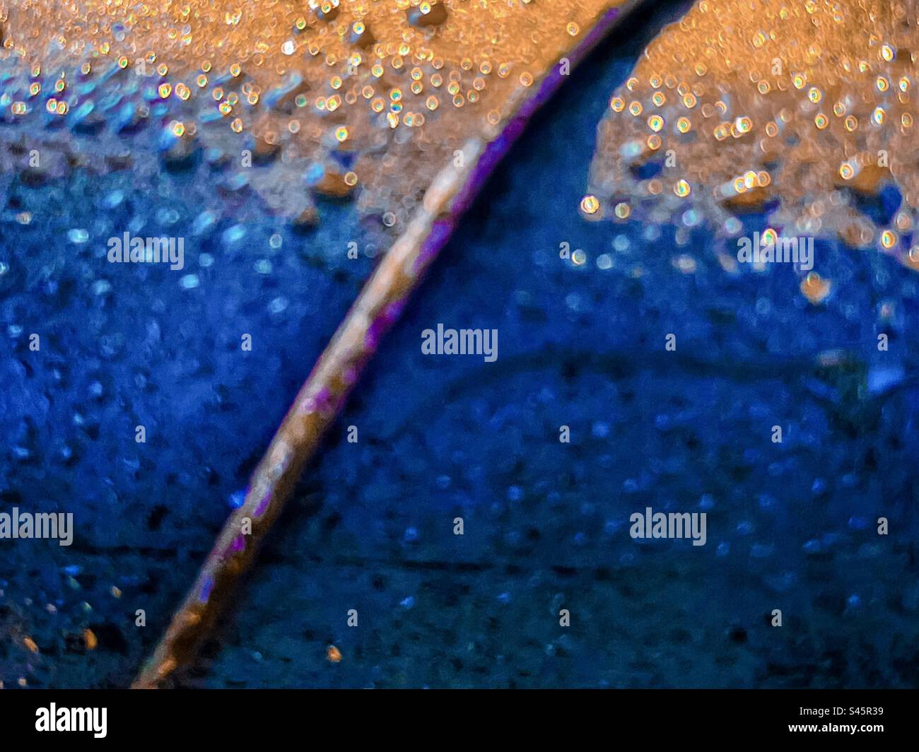 Close-up, abstract, full frame, backgrounds shot of rain droplets on metal surface in sunlight. Selective focus. Blue and golden colors. Texture. - Smartphone Captured Stock Image