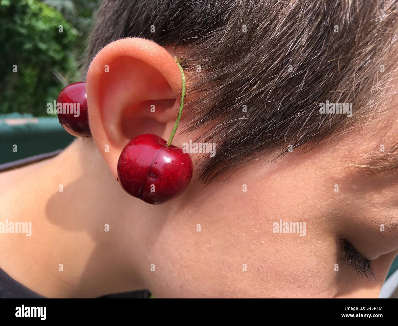 Child wearing a pair of cherry on his ear Stock Photo