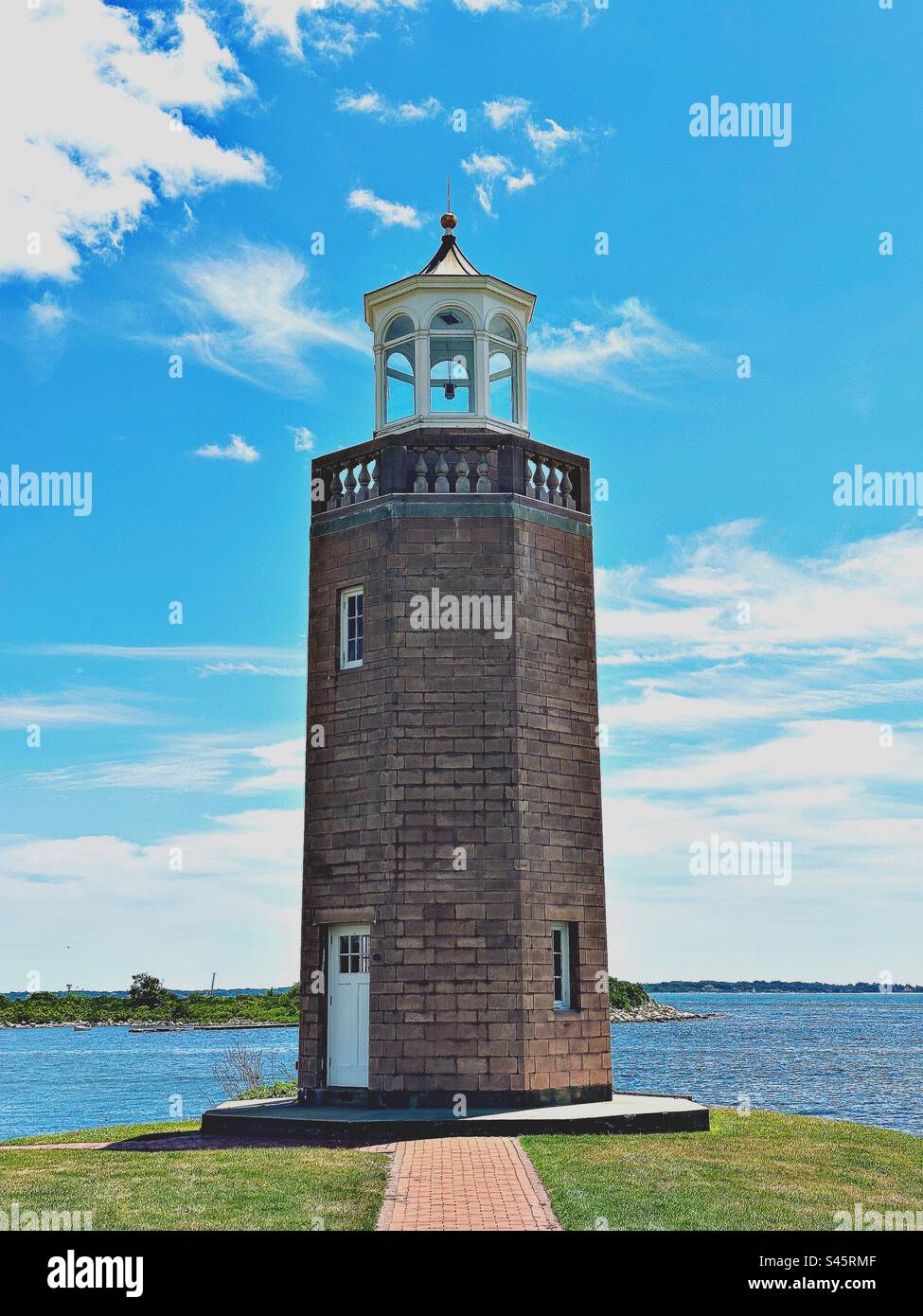 Avery Point Lighthouse on a summer day. Red brick path leading to building.  Water in the background in Groton, Connecticut, USA. - Smartphone Captured Stock Image
