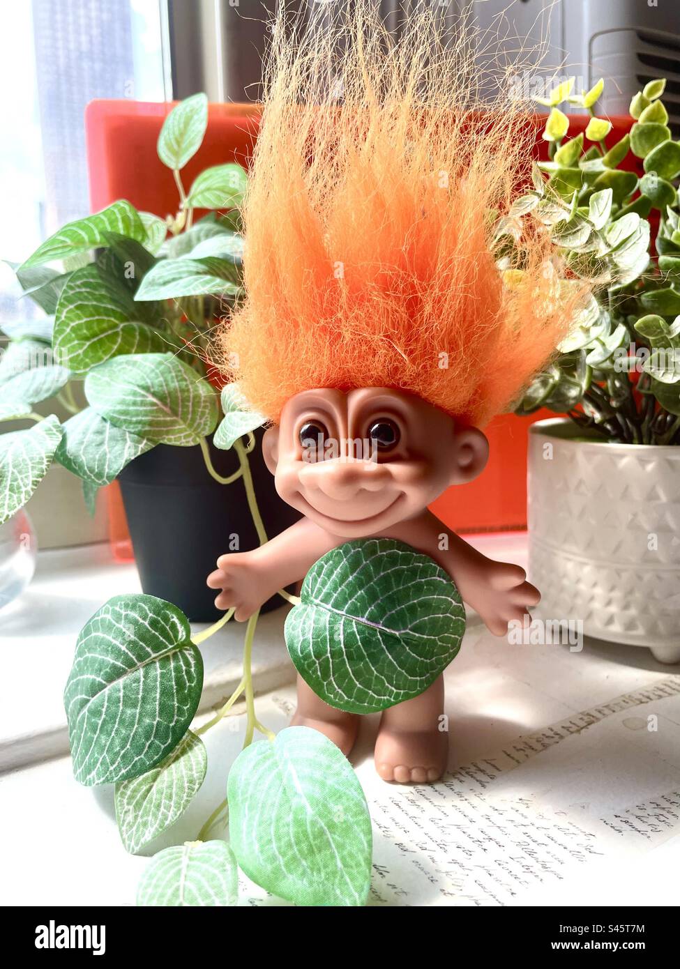 orange-haired troll doll among potted plants Stock Photo