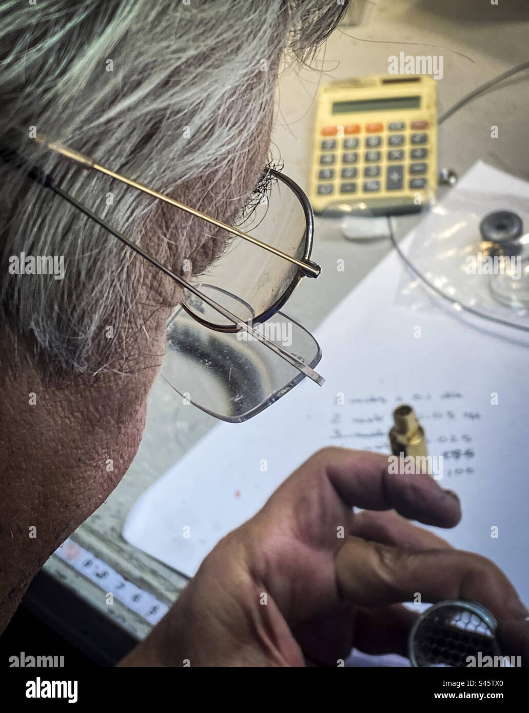An older man uses two pairs of glasses for an engineering project in the workplace - Smartphone Captured Stock Image