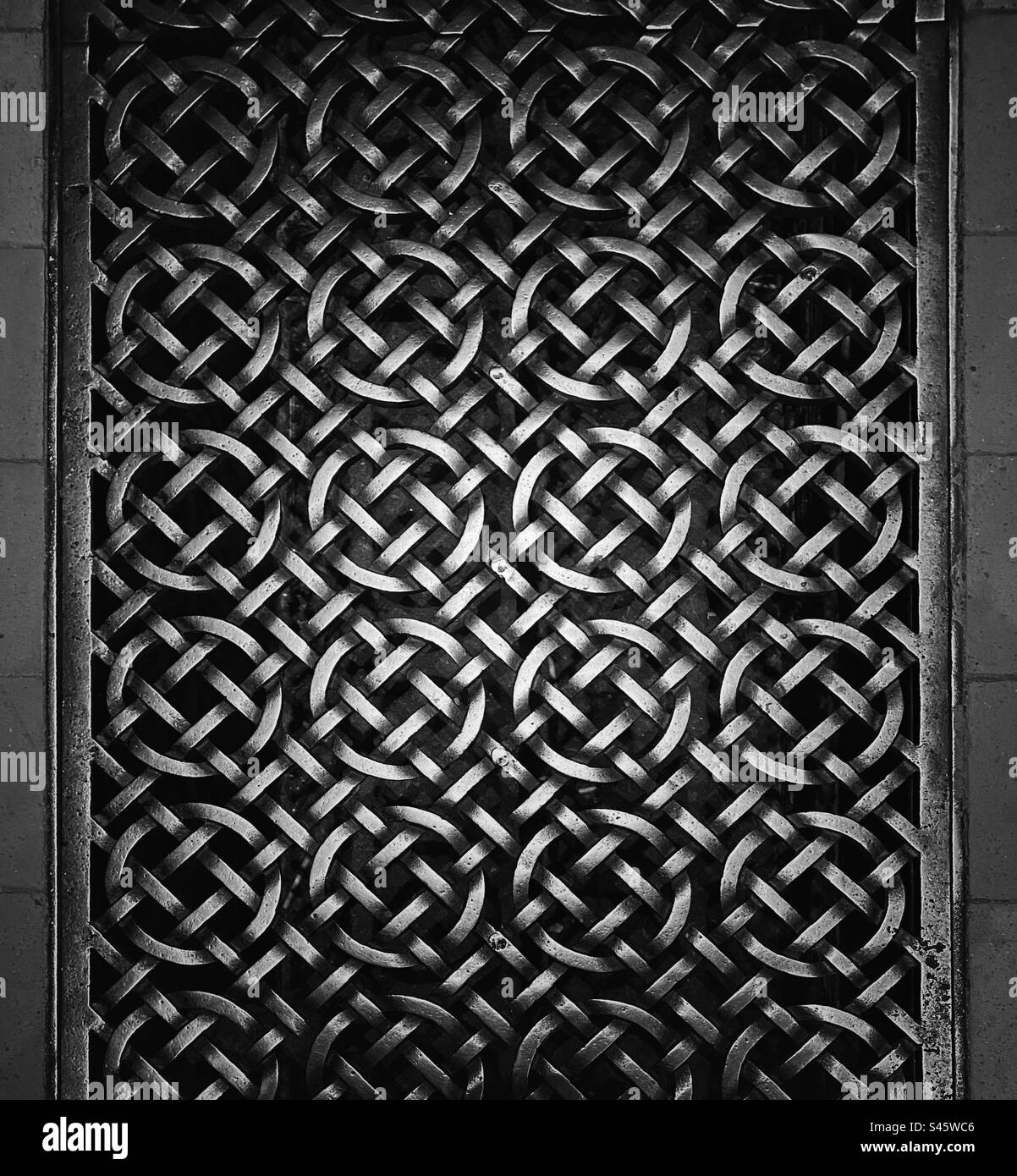 A photograph in black and white of a patterned metal floor grate