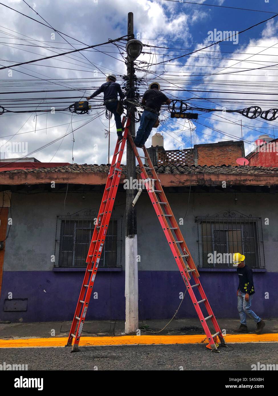 Two electricians staying on the stepladders doing cable work with another one on the ground, Xalapa, Mexico, 2022 - Smartphone Captured Stock Image