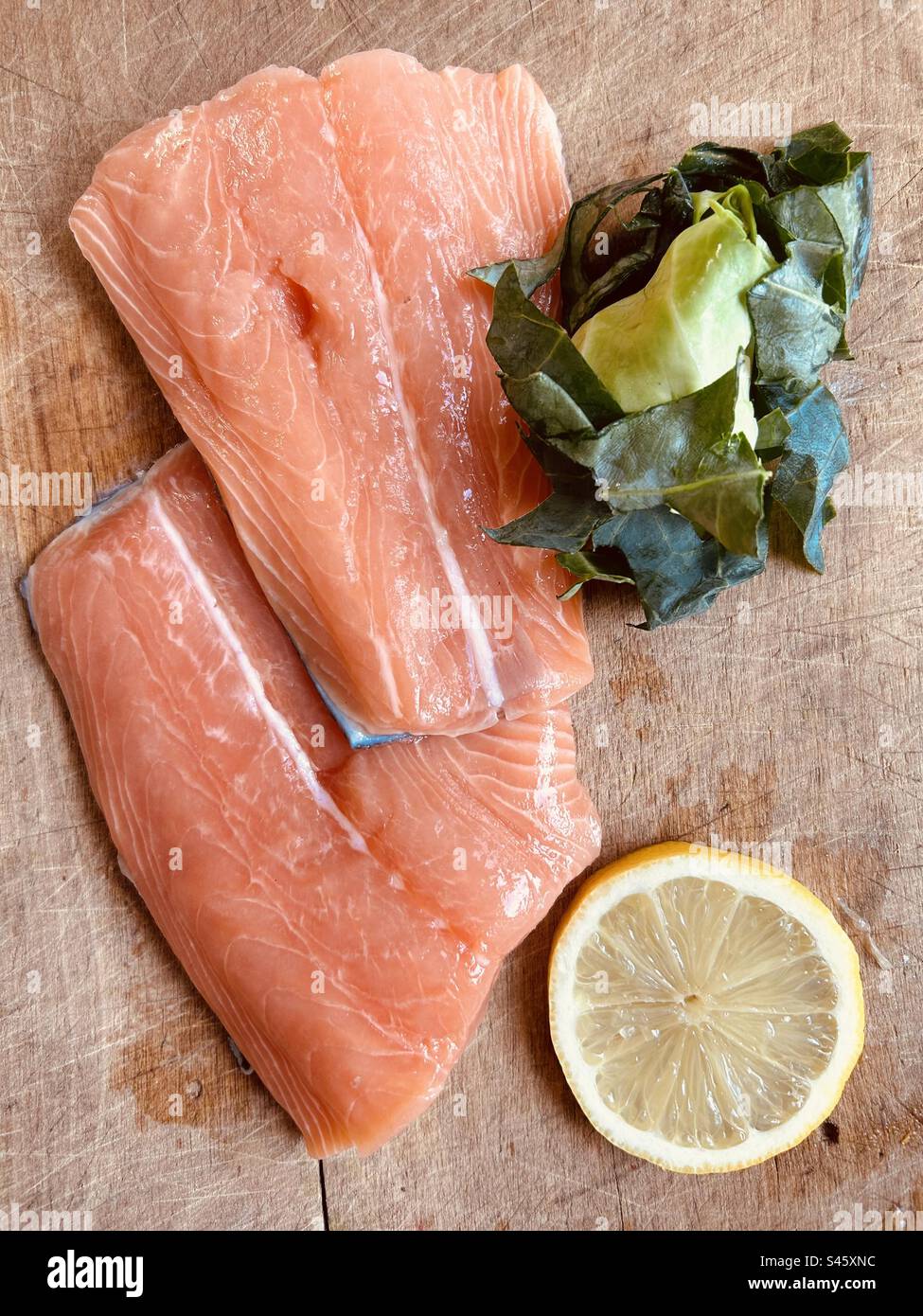 Fresh salmon tails, lemon slice and chopped green sweetheart cabbage on a wet chopping board. Ready  to cook. - Smartphone Captured Stock Image