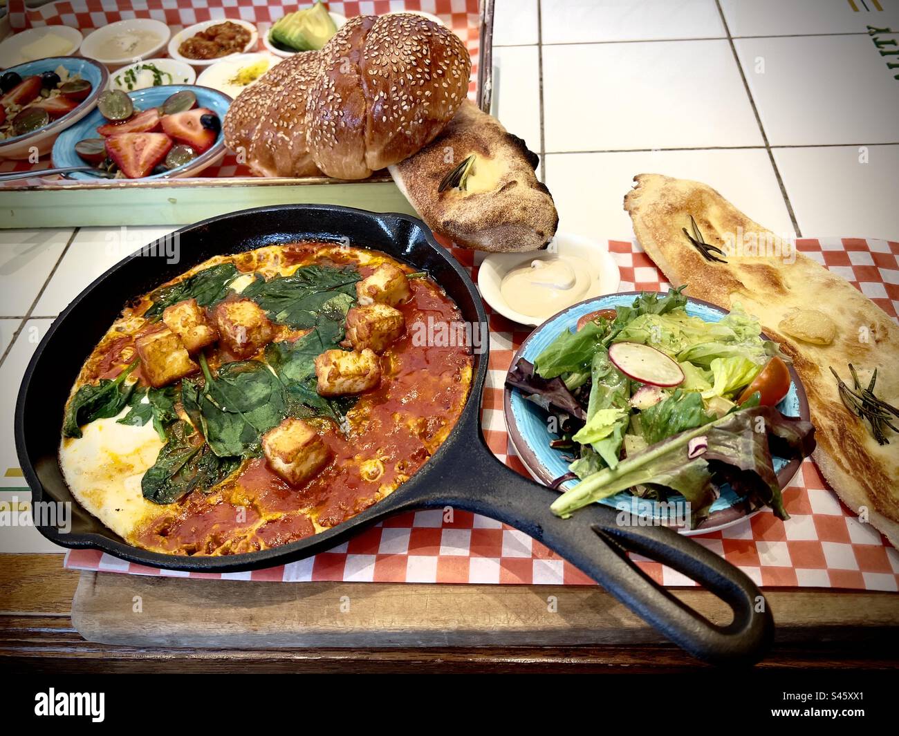 Amazing pan served table side of Shakshouka., salad and fresh bread including focaccia and challah in Toronto, Canada. - Smartphone Captured Stock Image