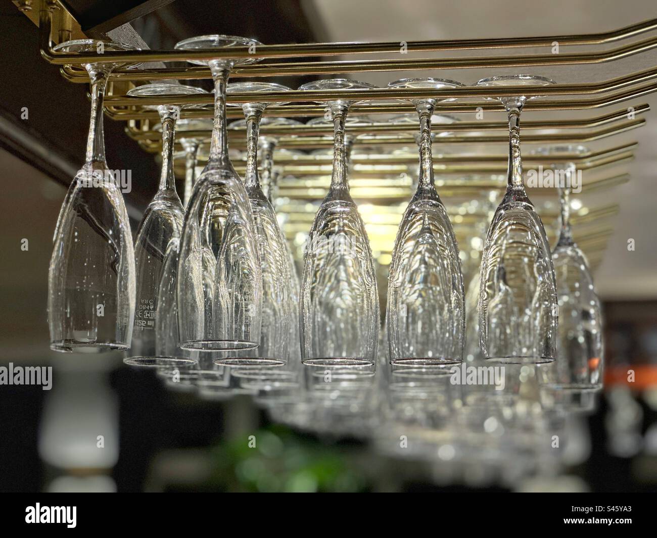 Champagne flutes hanging from a storage rack on top of a bar in a restaurant - Smartphone Captured Stock Image
