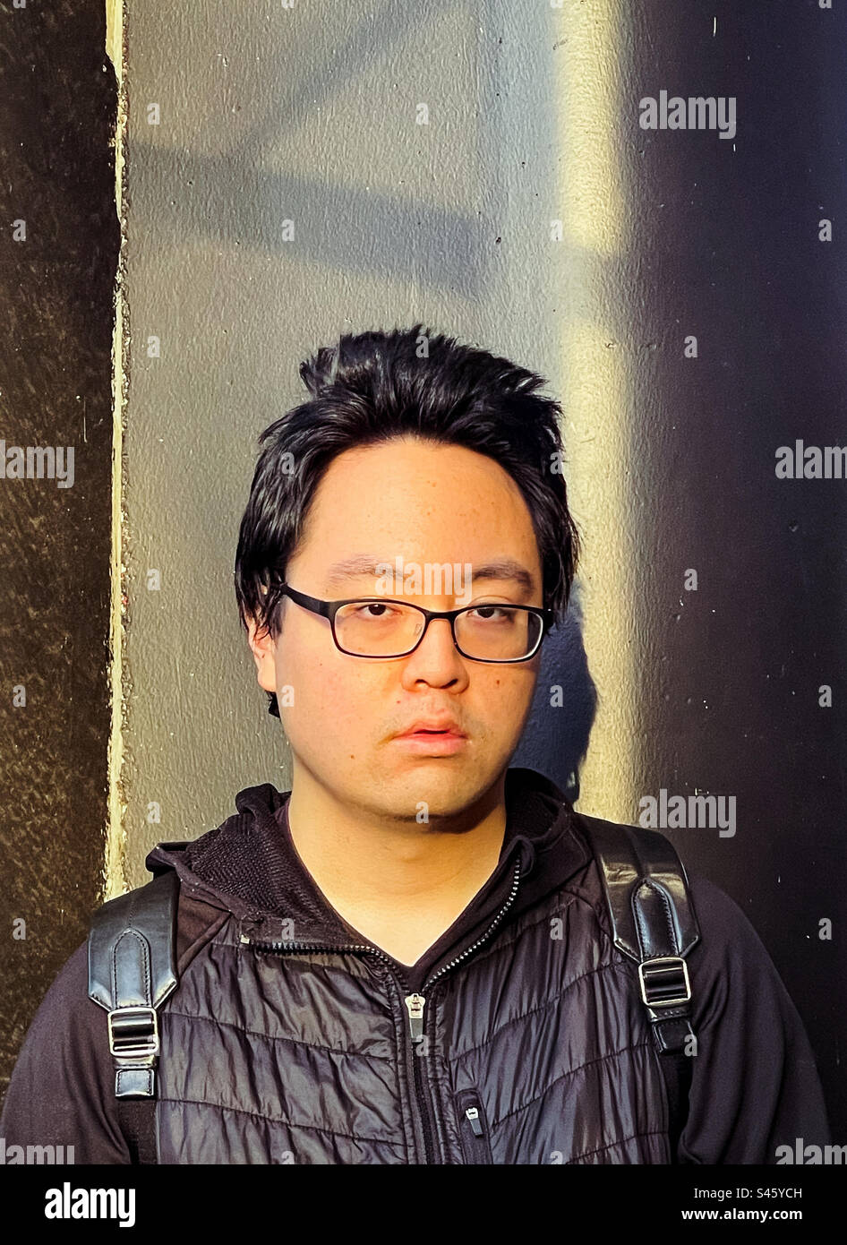 Portrait of young Asian man in eyeglasses against a wall. Vision care, hairstyle. Sunlight and shadows. - Smartphone Captured Stock Image