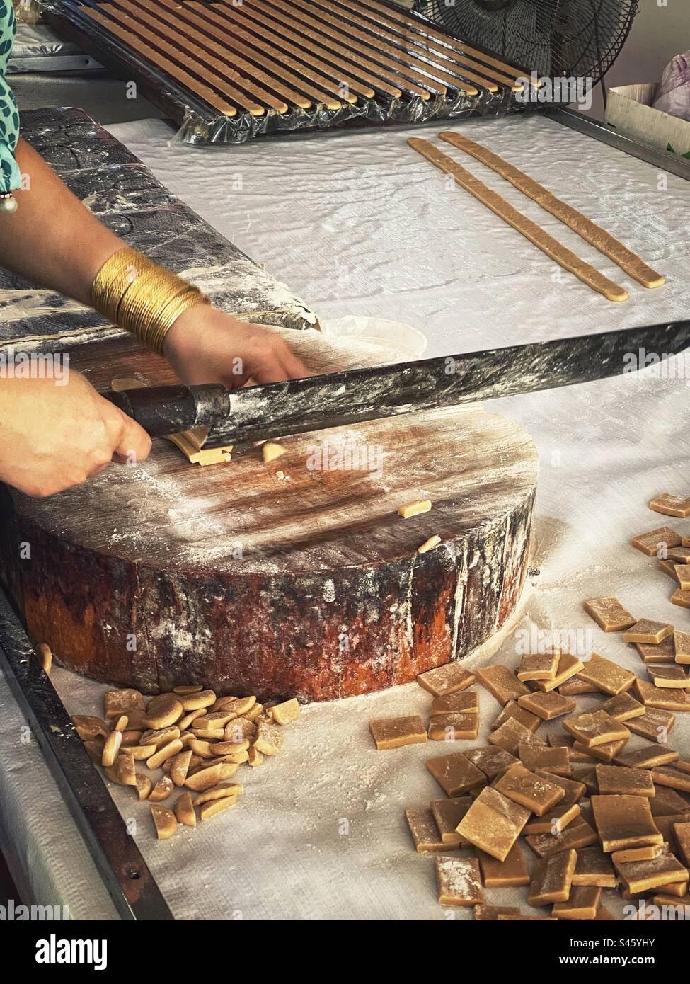 Vietnamese coconut candy factory. A  worker cutting coconut nougat strips into squares. - Smartphone Captured Stock Image