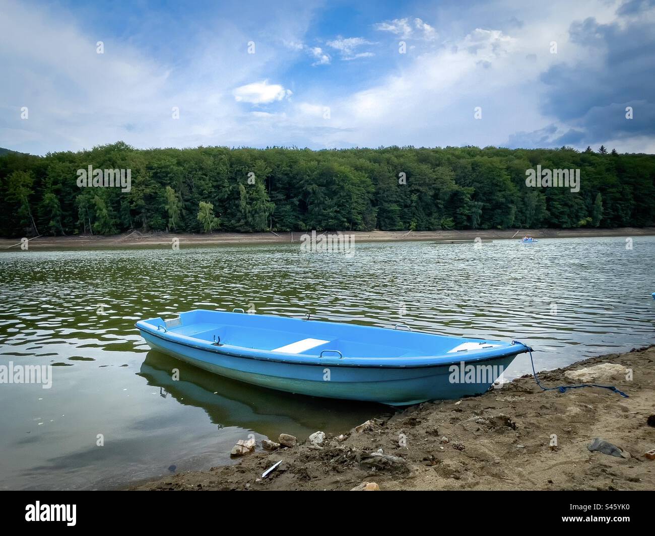 Blue wooden boat on a lake surrounded by green forest - Smartphone Captured Stock Image