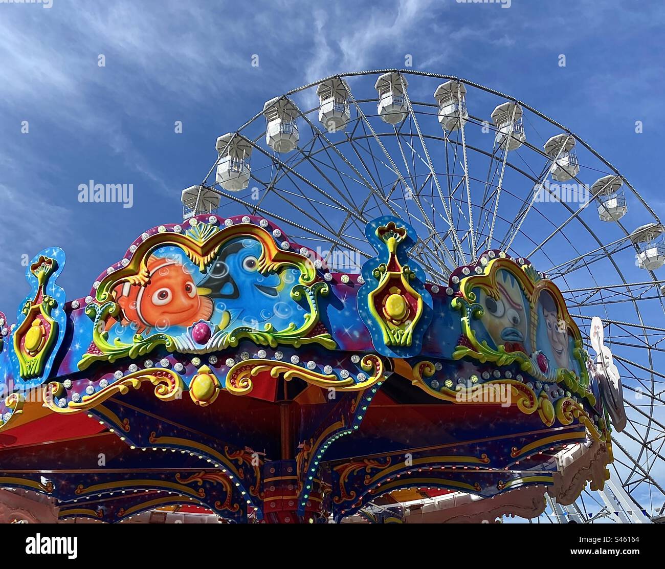 The decorative colour and shapes on the top of the children’s roundabout contrast with the simple white of the Big Wheel at Bangor, Northern Ireland. Many children’s activities surround the marina. Stock Photo