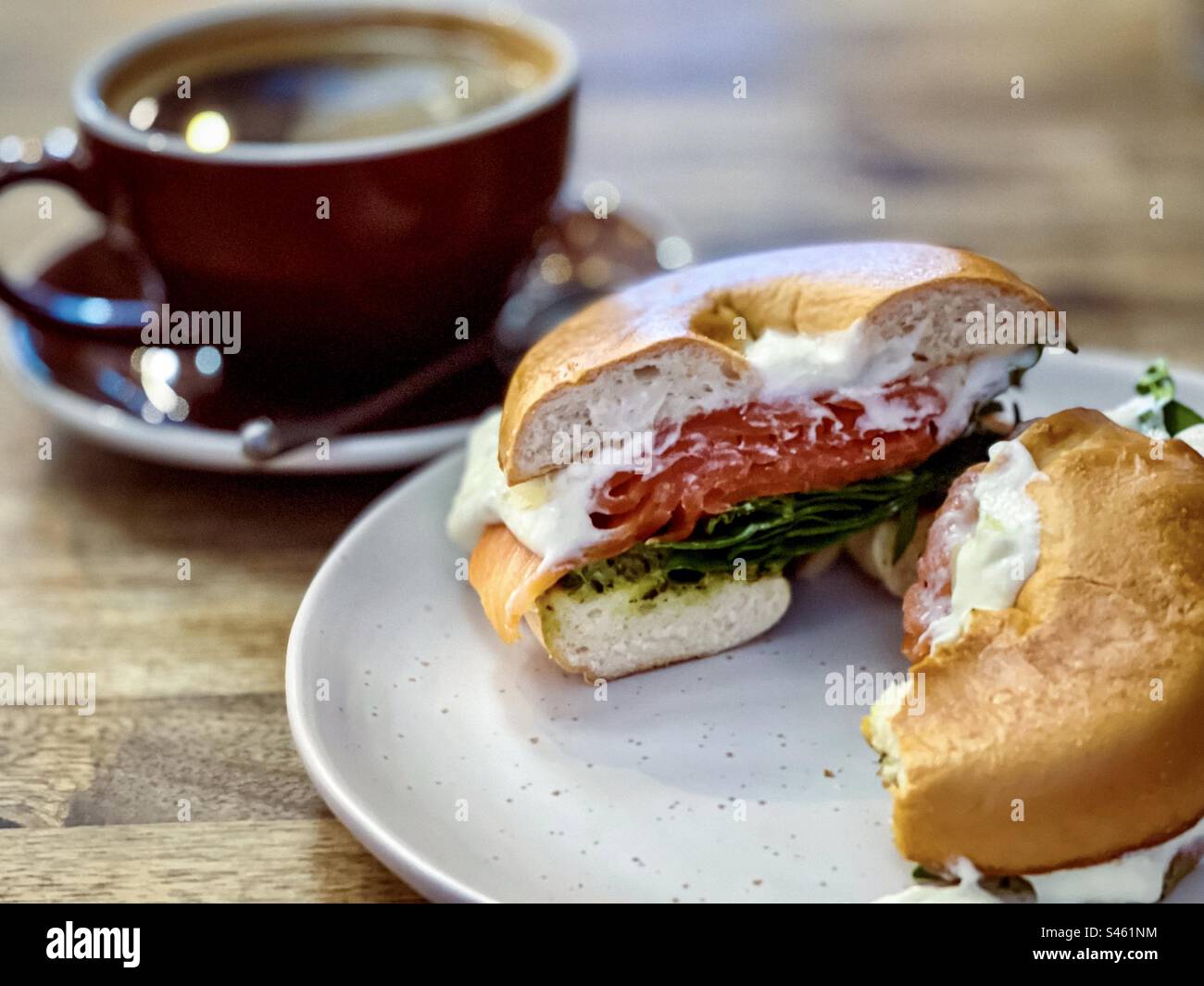 Close-up of salmon bagel with smoked salmon, spinach and tzatziki dip on plate and a cup of long black coffee on wooden table. - Smartphone Captured Stock Image