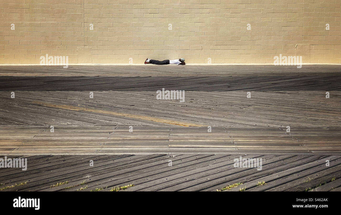 Man lying down at the edge of the boardwalk in Coney Island - Smartphone Captured Stock Image