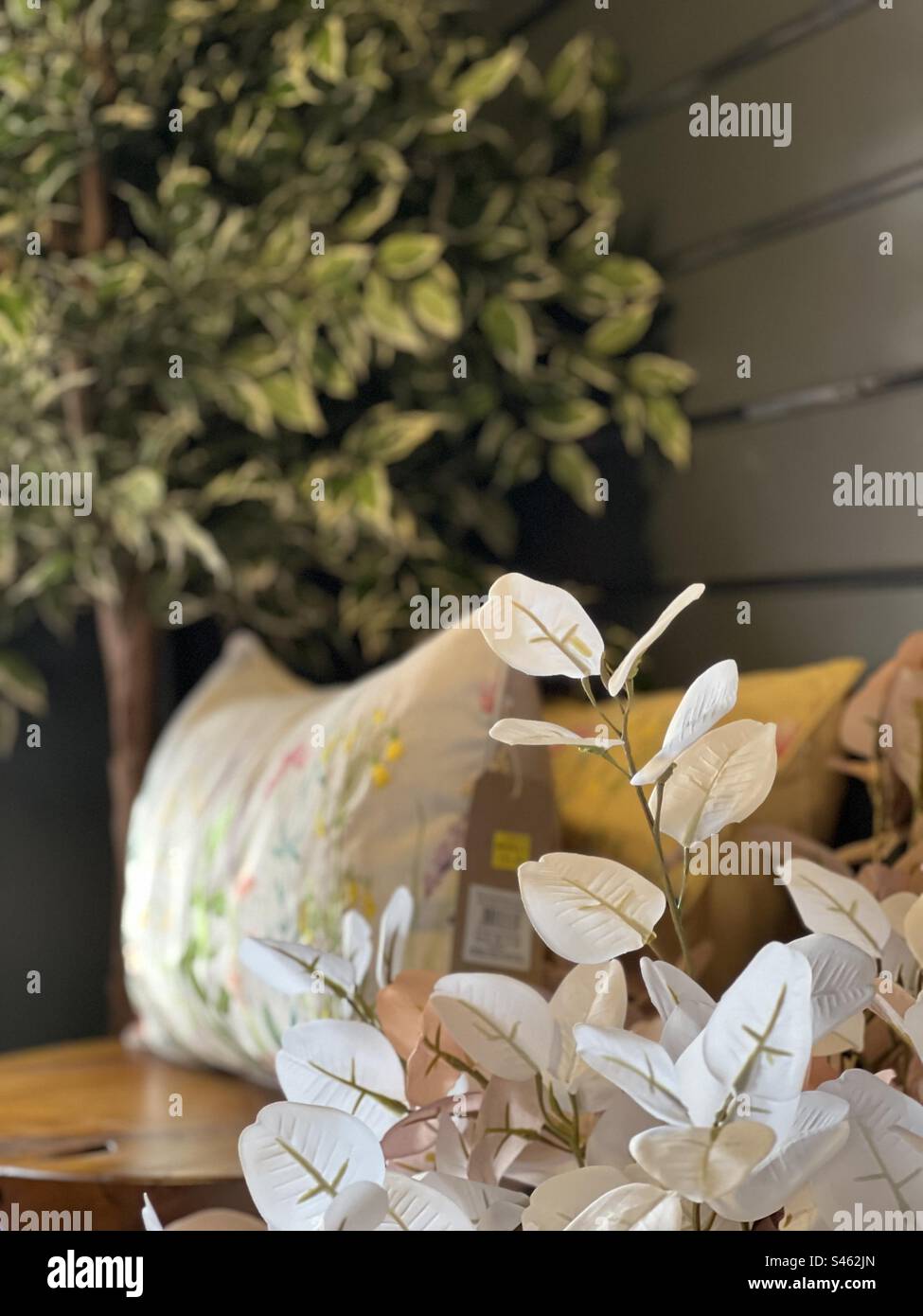 Interior design - mustard throw with a green leaved tree and a flowery cream cushion against a wooden panelled background Stock Photo