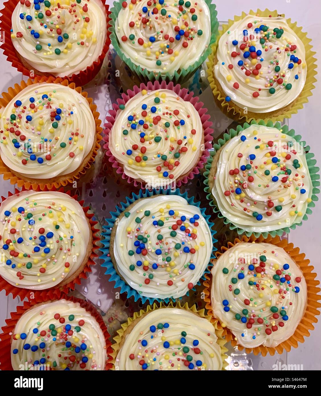 Rainbow coloured party fairy cakes with icing and sprinkles Stock Photo