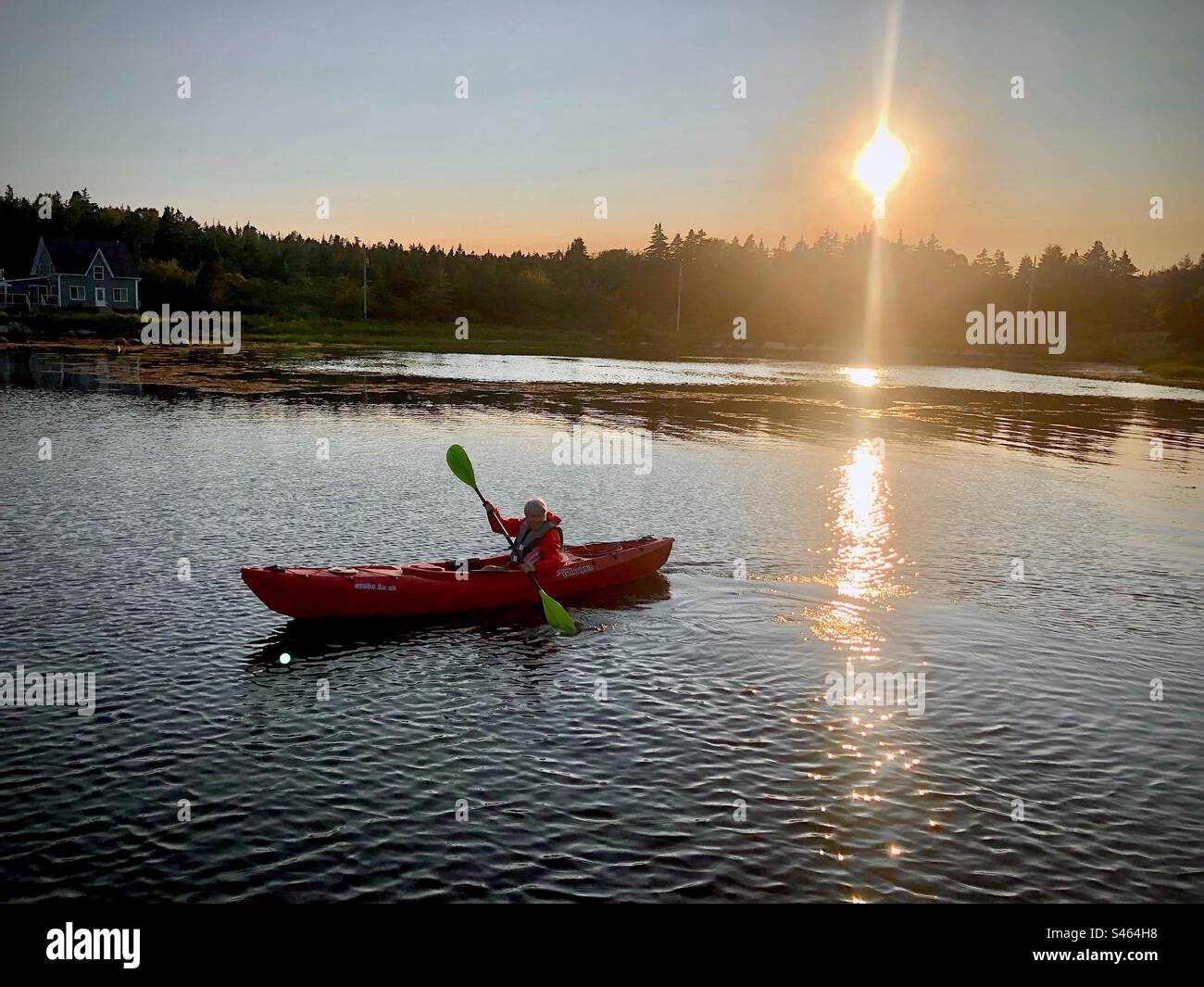 Kayaking solo at sunset. Senior. Woman. Paddle at sundown. Day’s end. Summer. Active . Independent. Alone. By herself. Outdoors. Adventure. - Smartphone Captured Stock Image