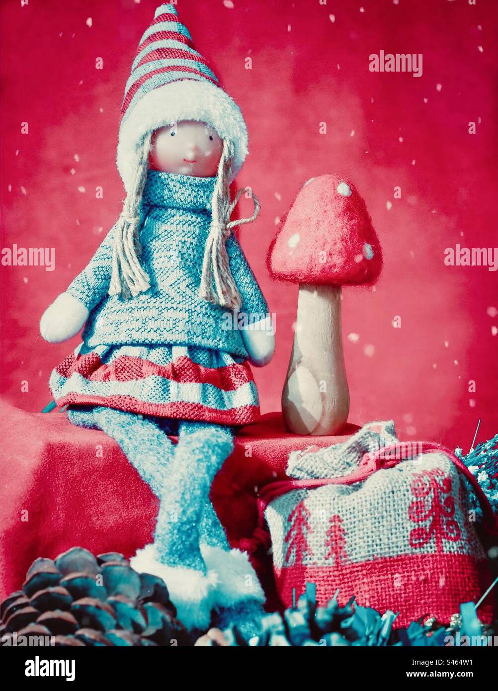 Christmasy doll sits with pinecones, present sack & mushroom in red with snowflakes - Smartphone Captured Stock Image