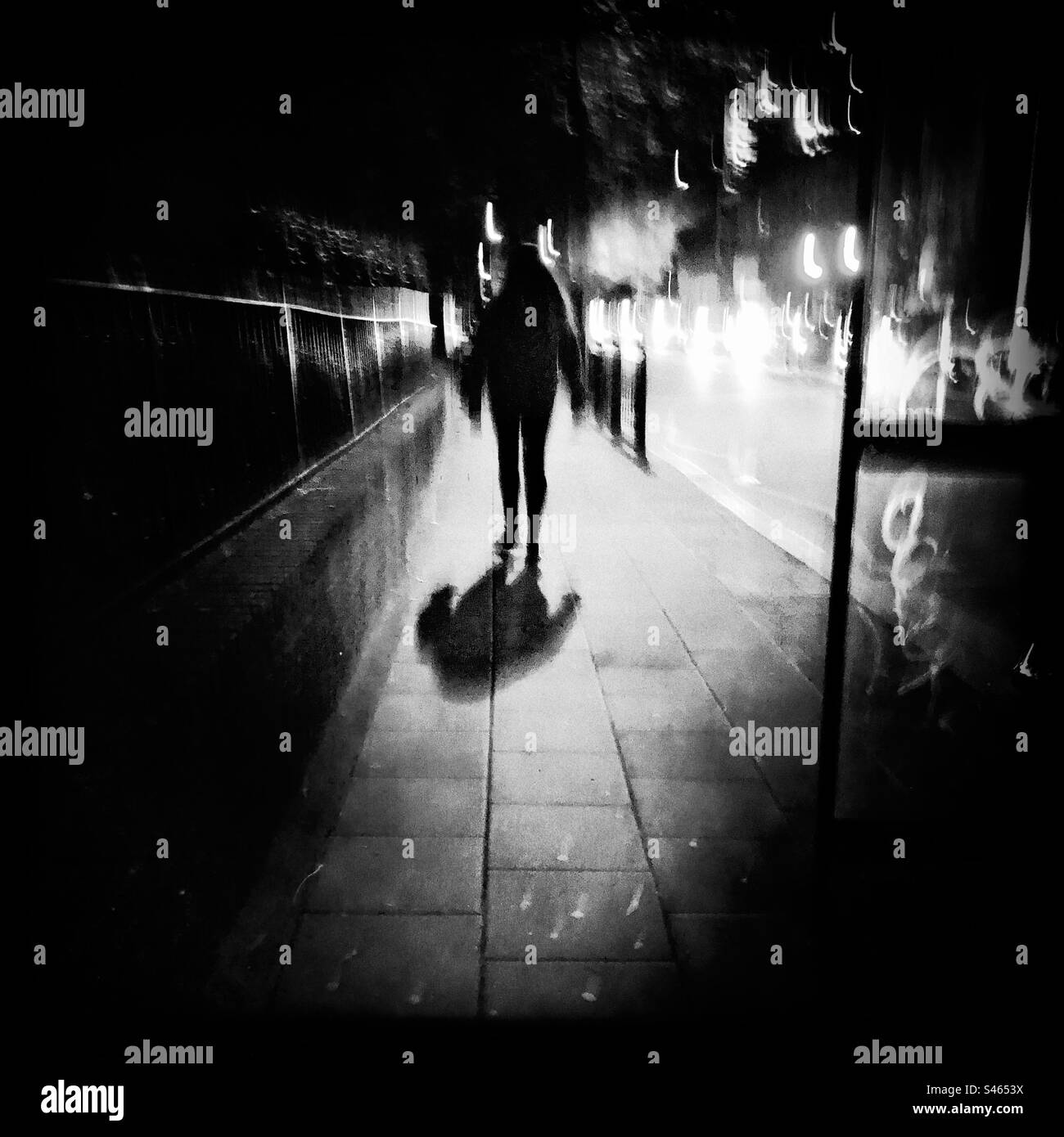 Silhouette of a woman waking on the pavement at night Stock Photo