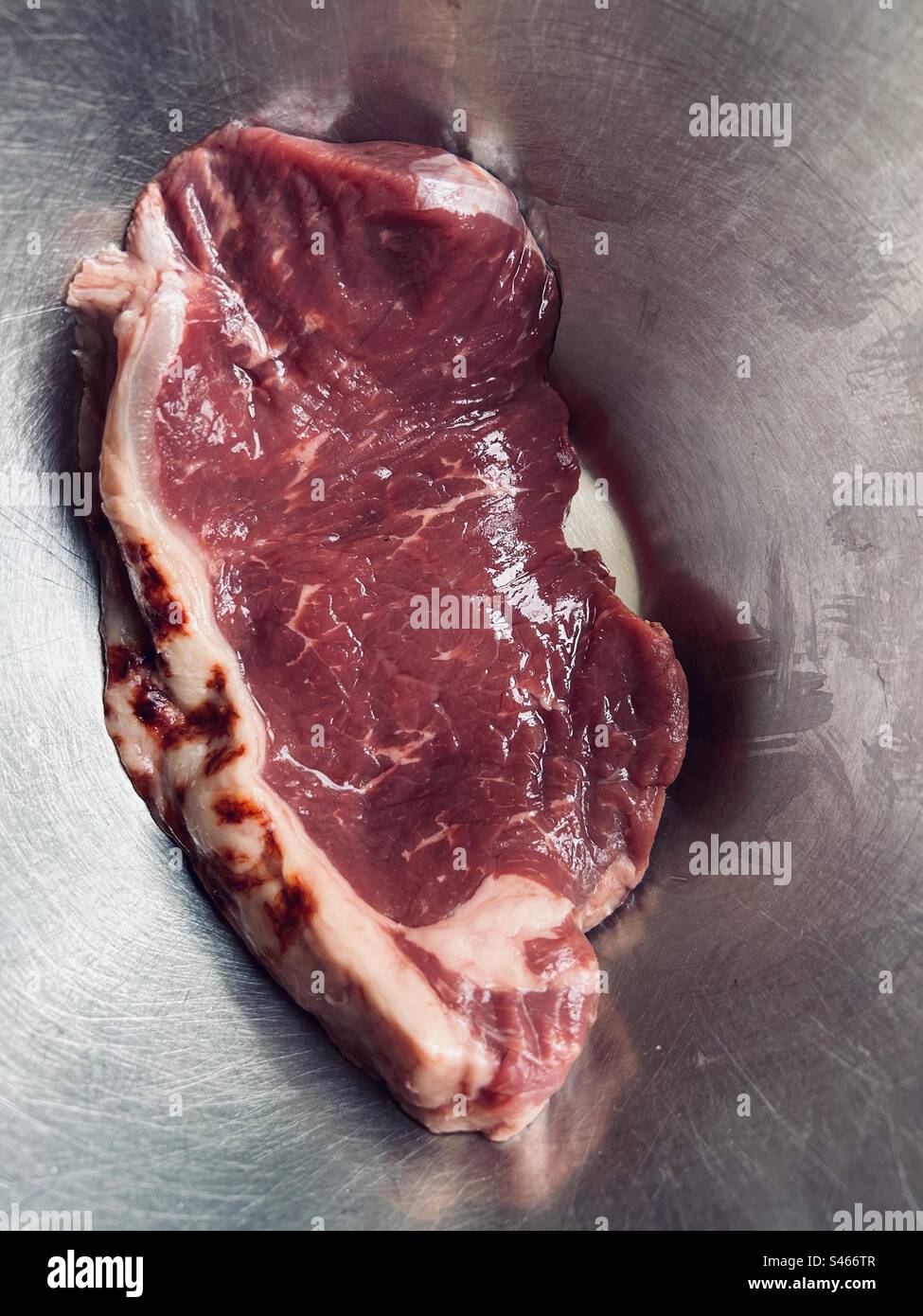 Red meat, ready for the frying pan. Raw sirloin steak, locally sourced. Crumpled. In a stainless steel bowl. - Smartphone Captured Stock Image