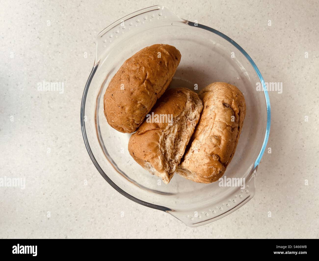 Our daily bread. Three freshly baked granary brown bread rolls in a glass bowl. Stock Photo