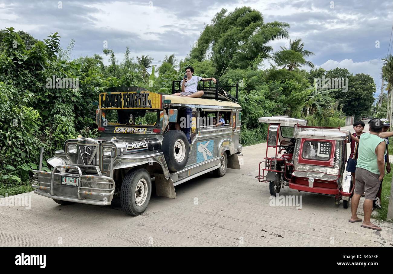 Jeepney passenger on the roof with his bed and a tricycle in rural province, Calabarzon region, Philippines Stock Photo
