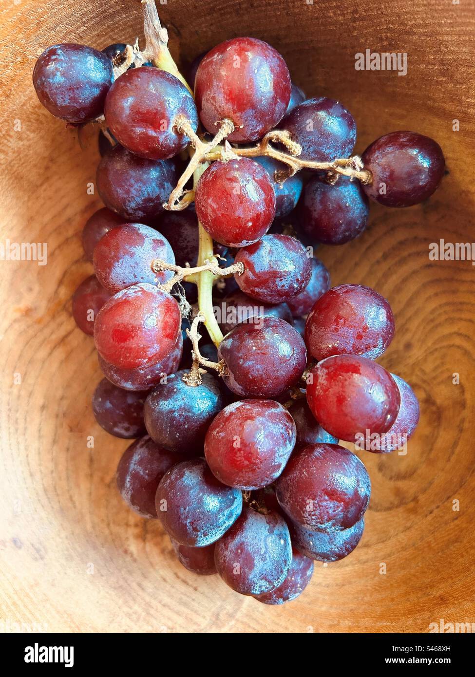Grapes in a grained wooden bowl. One bunch. Red grapes, fresh and juicy. Stock Photo