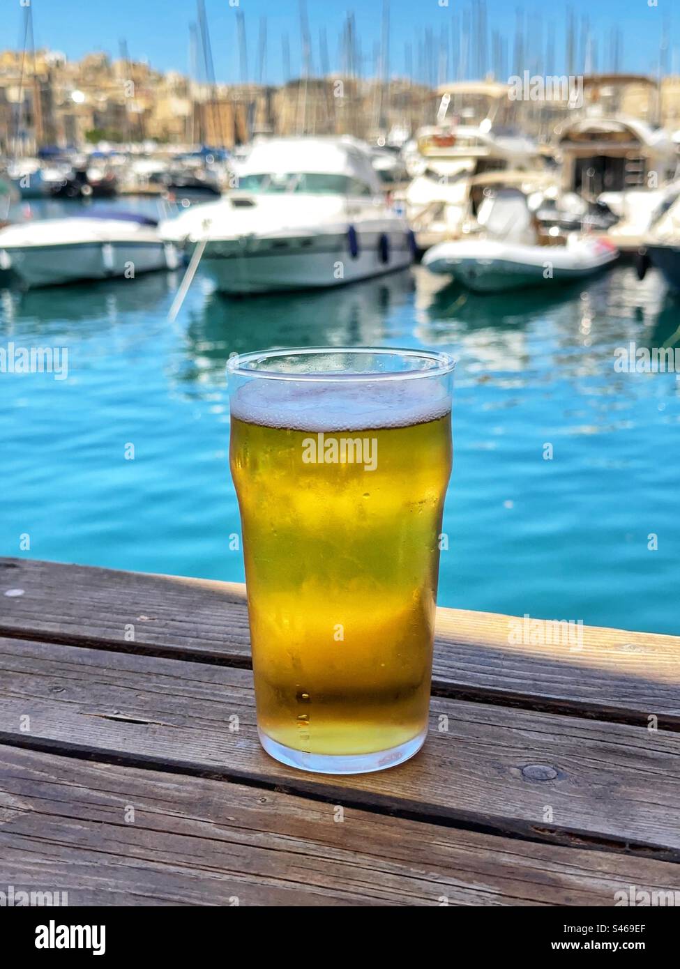Glass of cold beer on a table in a bar overlooking boats in a marina in Three Cities in Valletta, Malta - Smartphone Captured Stock Image