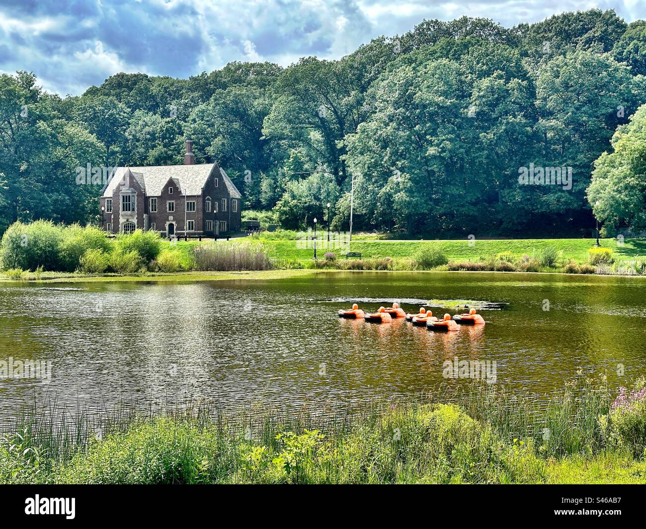 Park View Room building in the distance as seen from Elm Park in historic downtown Worcester, Massachusetts, USA.  Art installation with orange shaped floating “people” in the pond on a summer day. - Smartphone Captured Stock Image