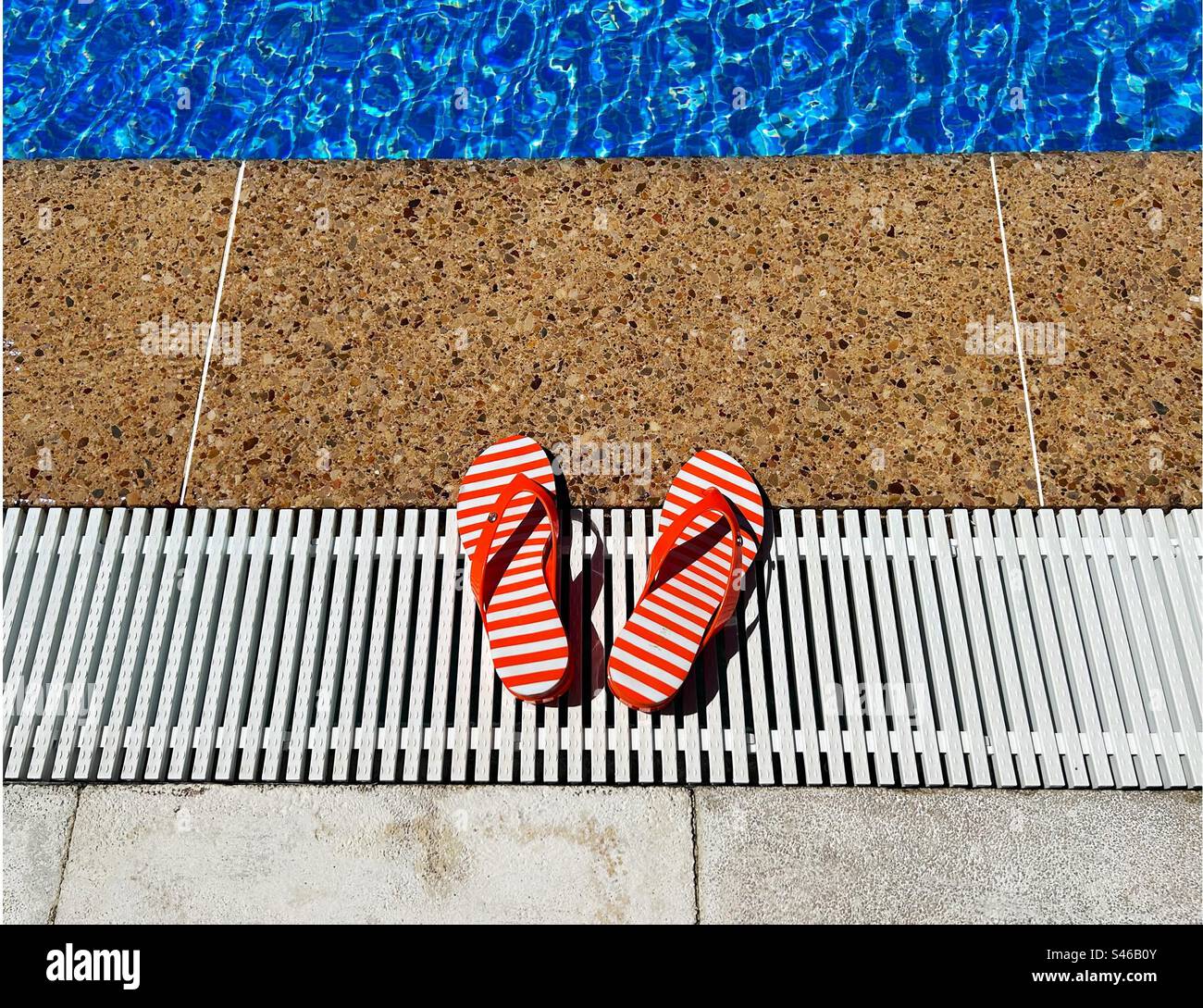 Red and white striped flip flops by the edge of a swimming pool Stock