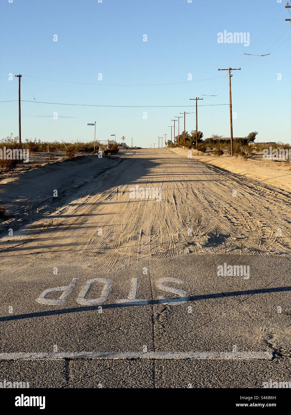 Stop sign on tarmac at the end of a dirt road through the desert in Southern California. Telegraph poles disappear into the distance - Smartphone Captured Stock Image