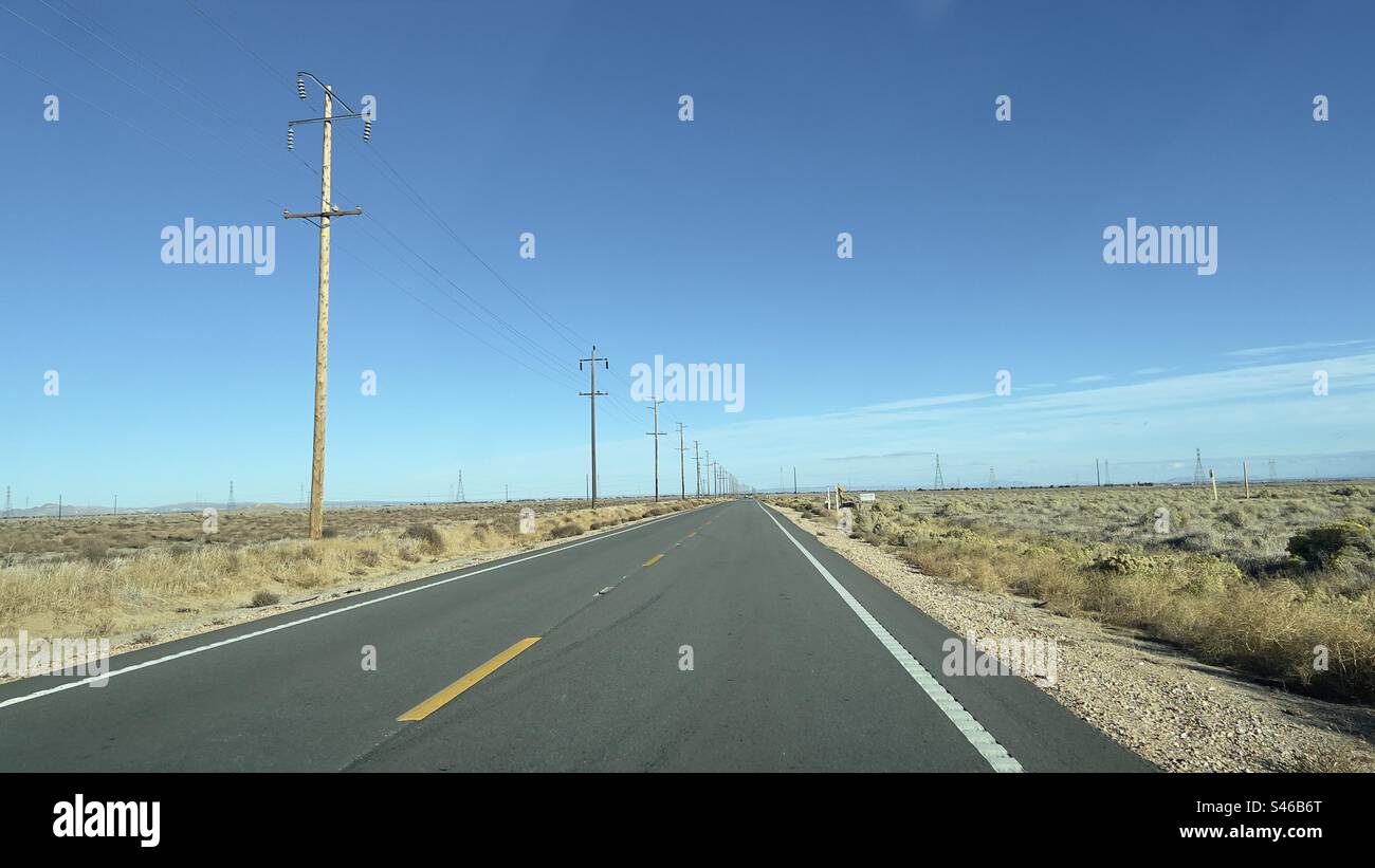 Wide view desert highway leading to distant mountains, yellow markings on asphalt, telephone poles on the left and blue sky overhead. California, day time - Smartphone Captured Stock Image