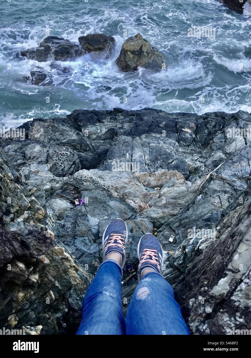 A lonely girl looking down from the top rock looking to the sea - Smartphone Captured Stock Image