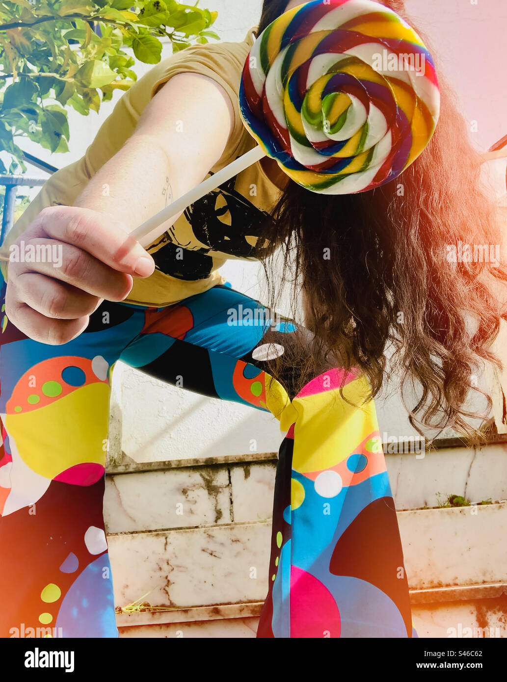 Woman in psychedelic flare holds colourful lollipop outstretched toward the camera - Smartphone Captured Stock Image