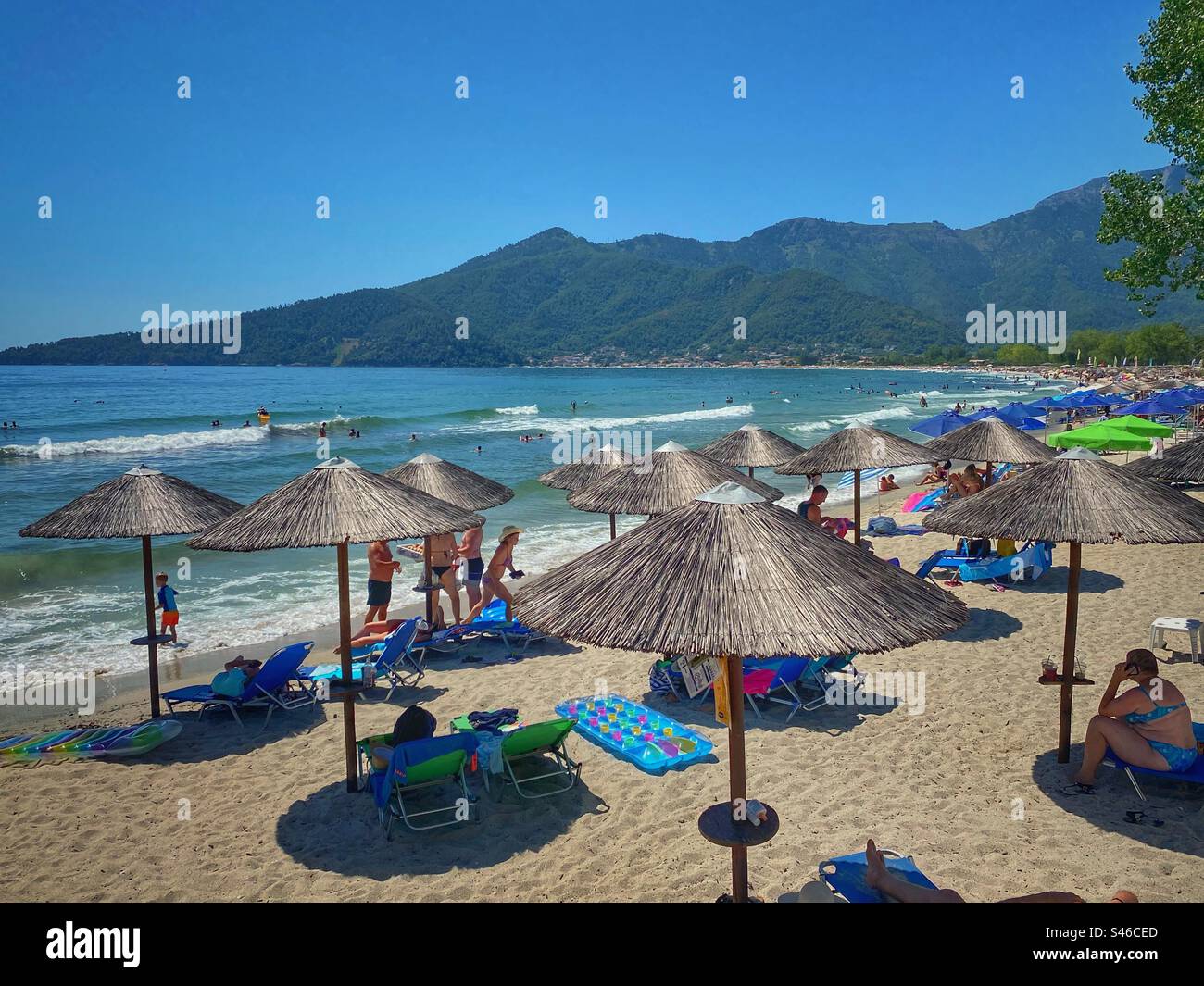 Sea view with sun umbrellas and green gills at Golden Beach on Thassos island, Greece. - Smartphone Captured Stock Image