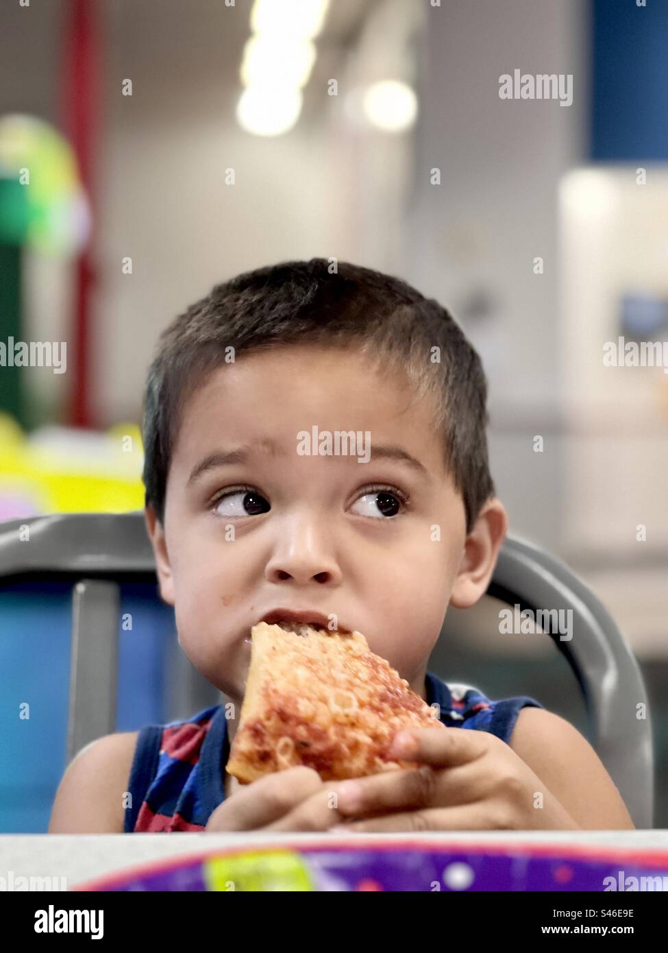 A cute little dark haired boy eating pizza in a restaurant Stock Photo