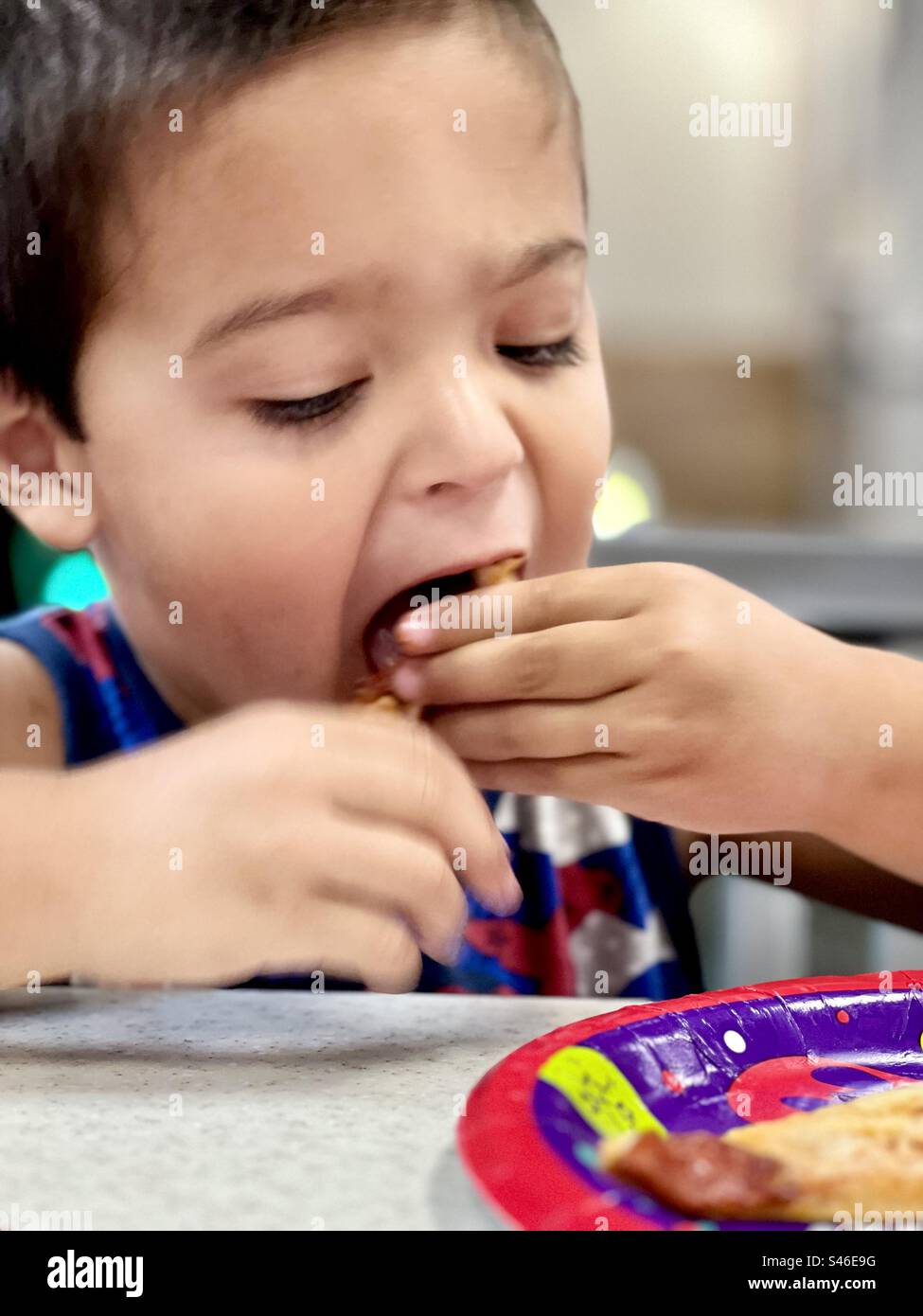 Young boy with dark hair eating in a restaurant using his hands Stock Photo