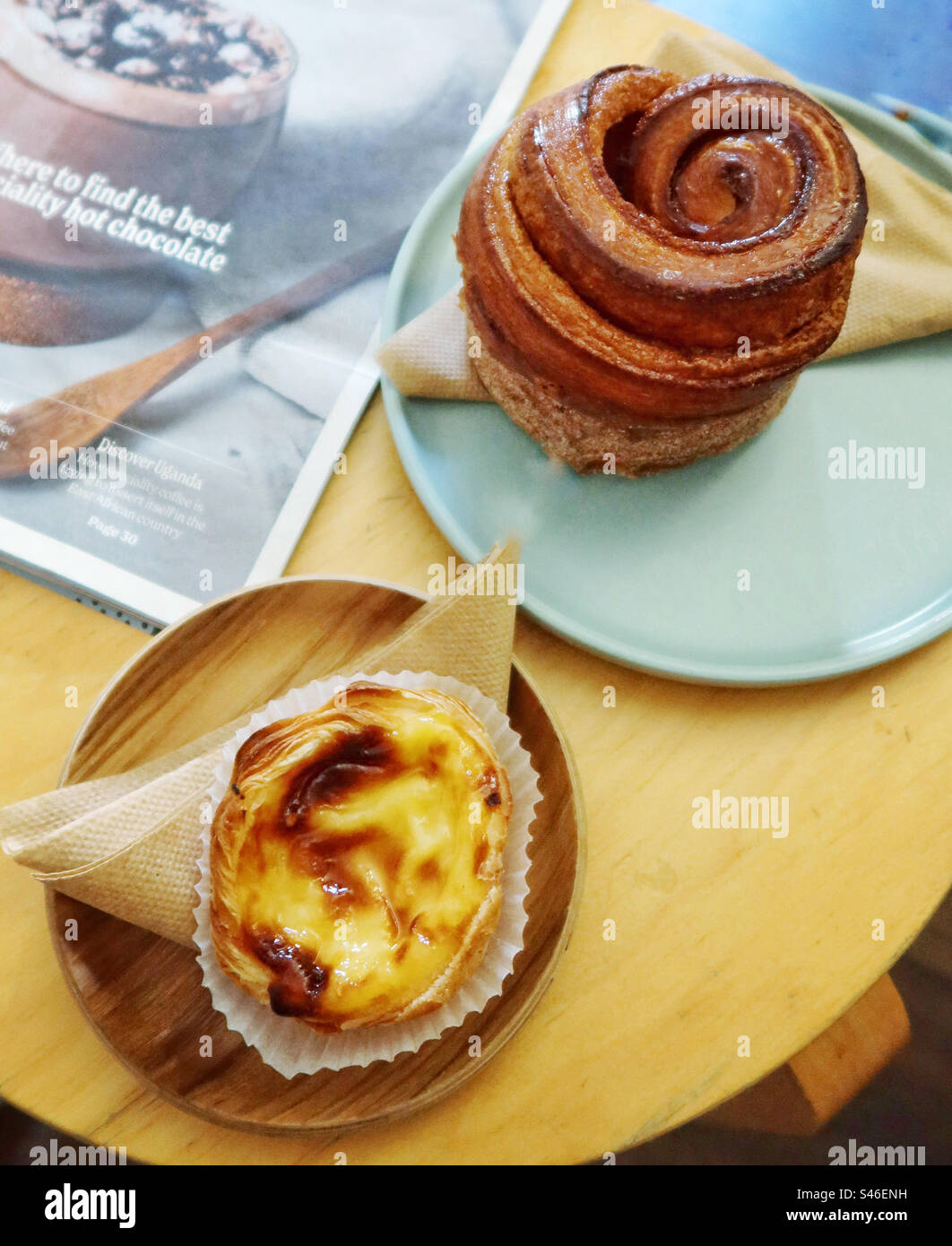 Custard tart, pastel de nata, and a cinnamon bun on plates on a table with a magazine - Smartphone Captured Stock Image
