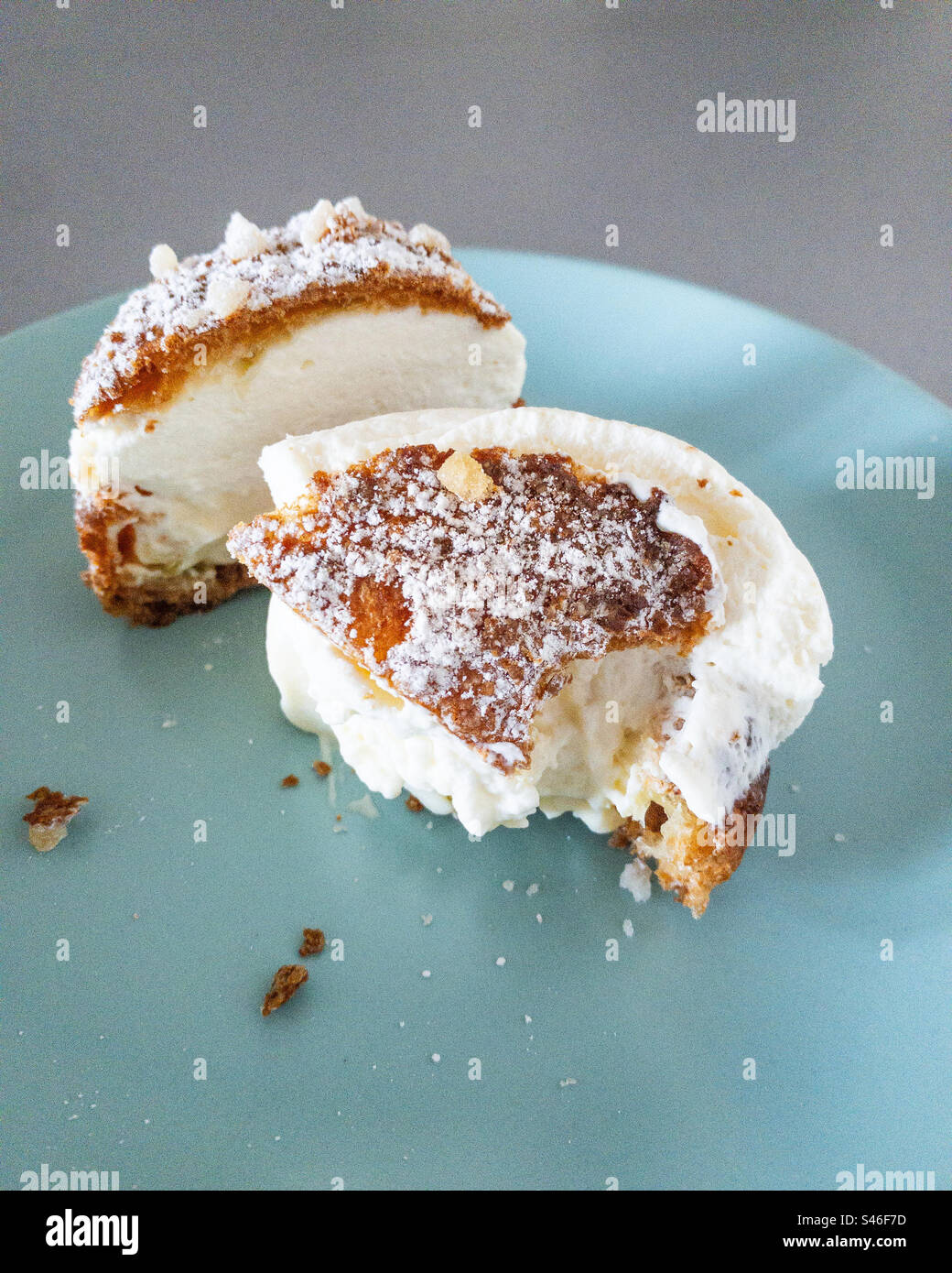Creme puff on turquoise plate, cut in half and partially eaten with crumbs. - Smartphone Captured Stock Image