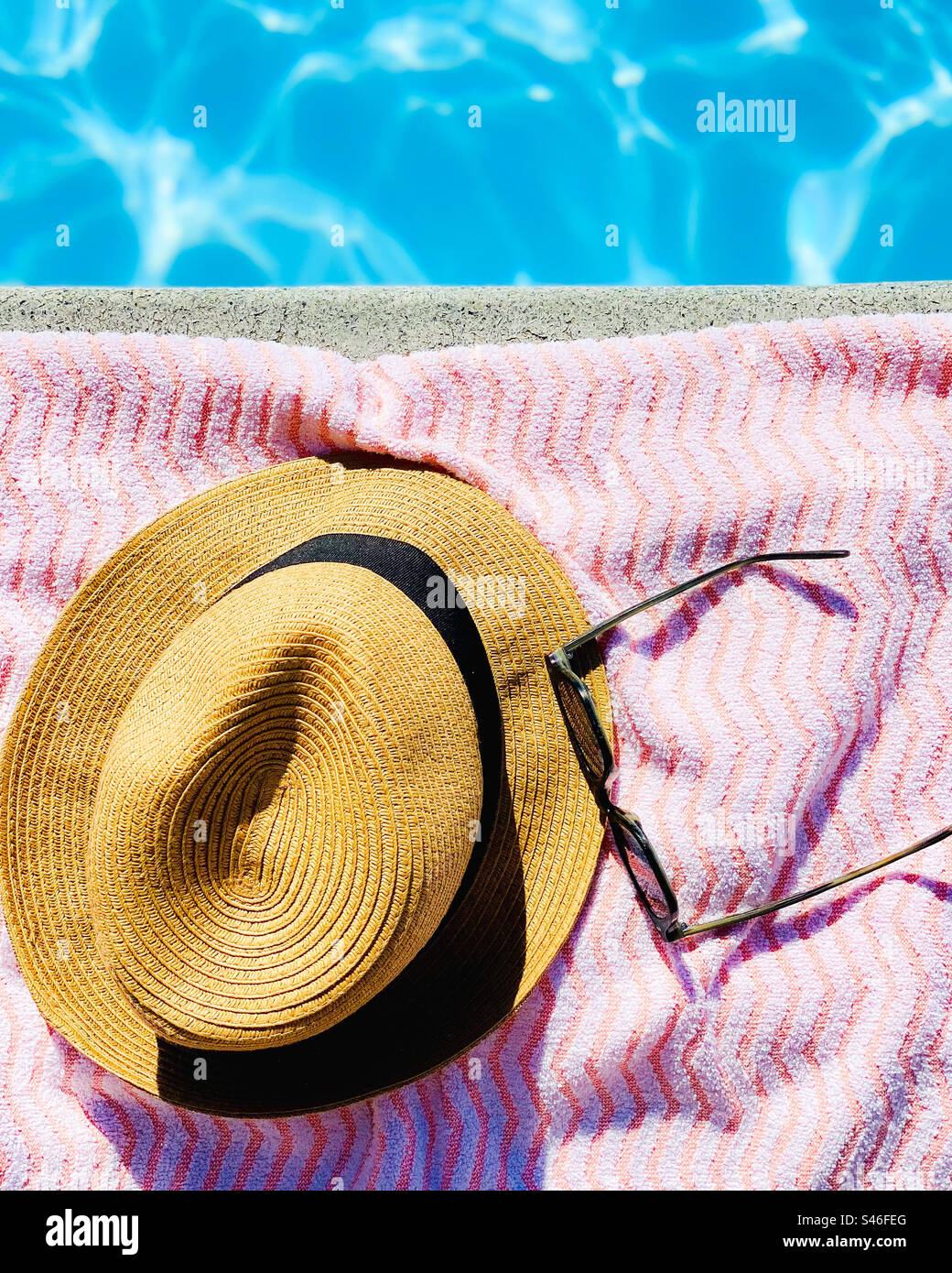 Straw hat and sunglasses on a beach towel beside a swimming pool in the summer. - Smartphone Captured Stock Image