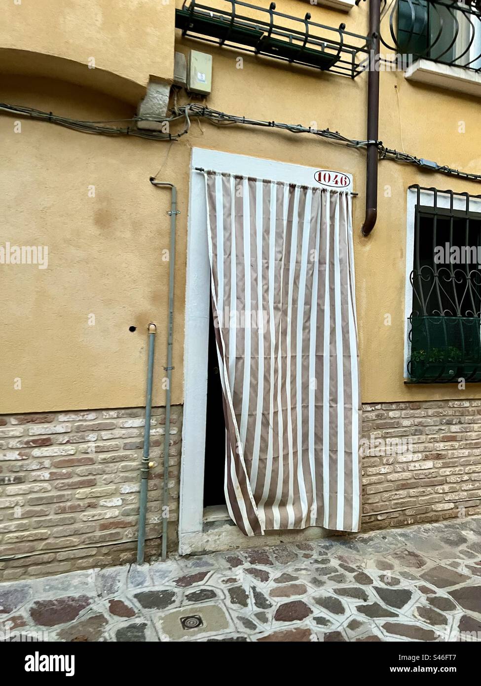 Brown and white stripe fabric covers an entryway to a canal home in Sestiere Cannaregio, Venice - Smartphone Captured Stock Image