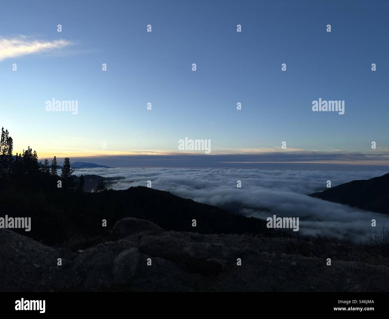 Looking down on low clouds as they roll in below silhouetted mountain peaks at sunset - Smartphone Captured Stock Image