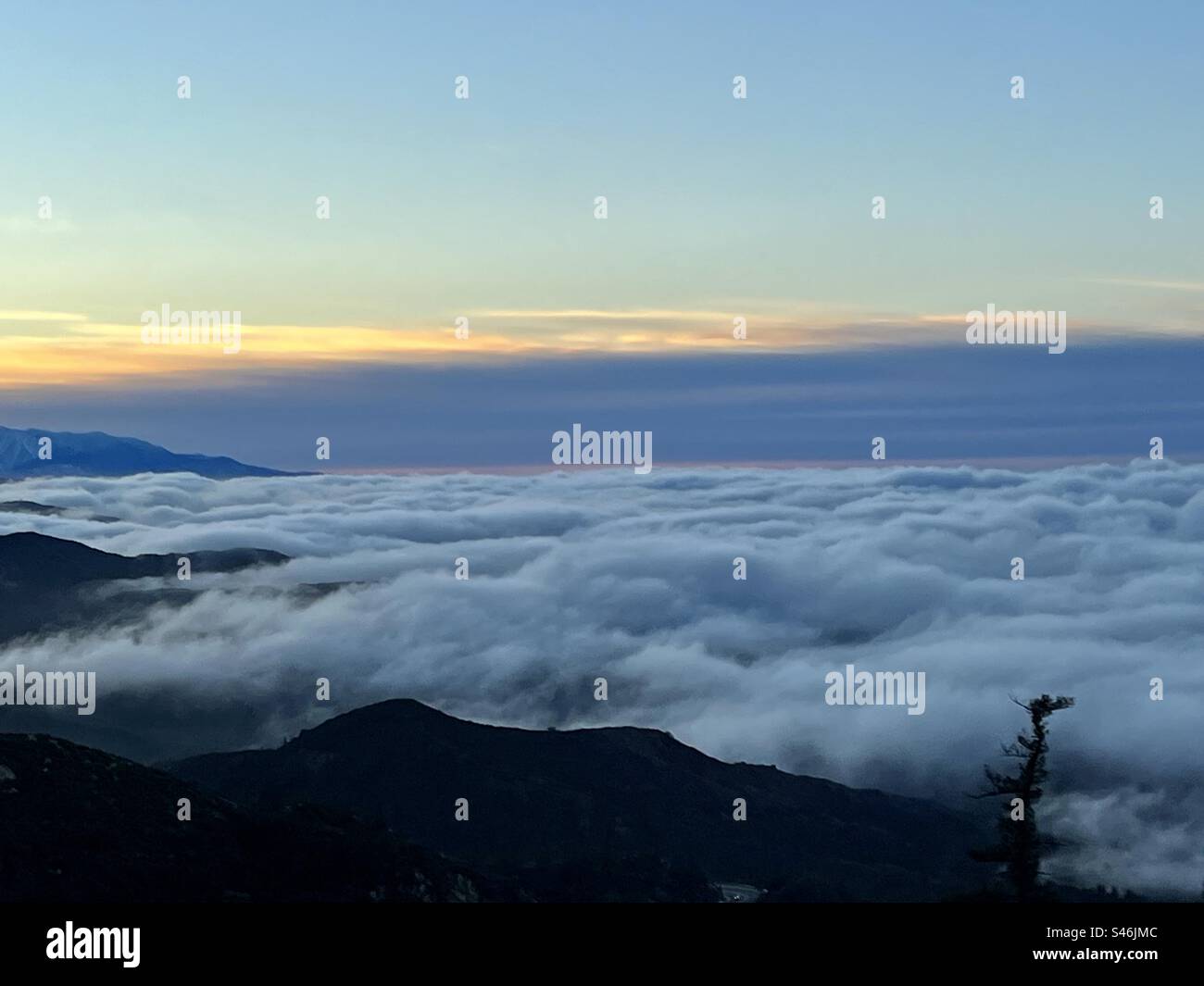 Silhouetted mountains and trees with low clouds rolling in, below the peaks at sunset - Smartphone Captured Stock Image