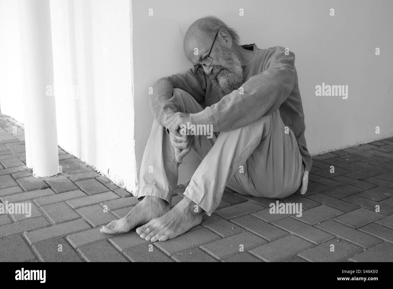 Senior homeless sitting in town Stock Photo