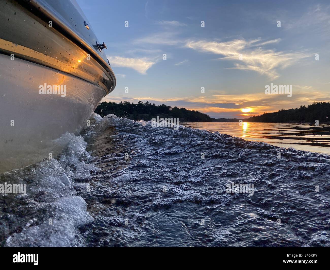 Boat cutting through water into a sunset, low angle - Smartphone Captured Stock Image