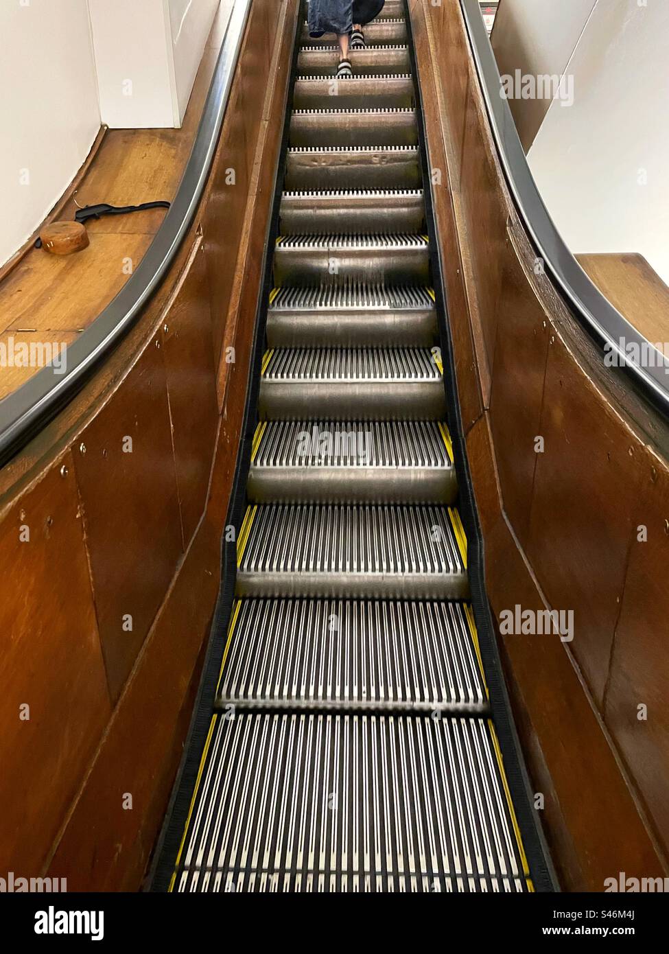 Woman using an up escalator with ornate wooden hand rails, 2023, USA - Smartphone Captured Stock Image