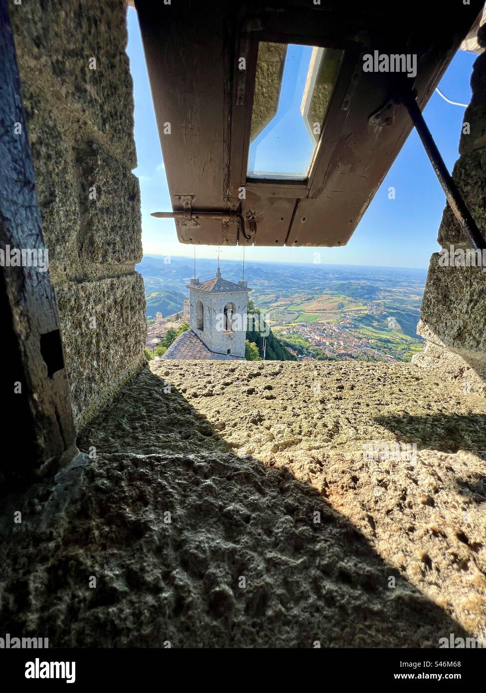 Stone sill and wooden shutter propped open in Guaita fortress, exposing a colorful San Marino below - Smartphone Captured Stock Image