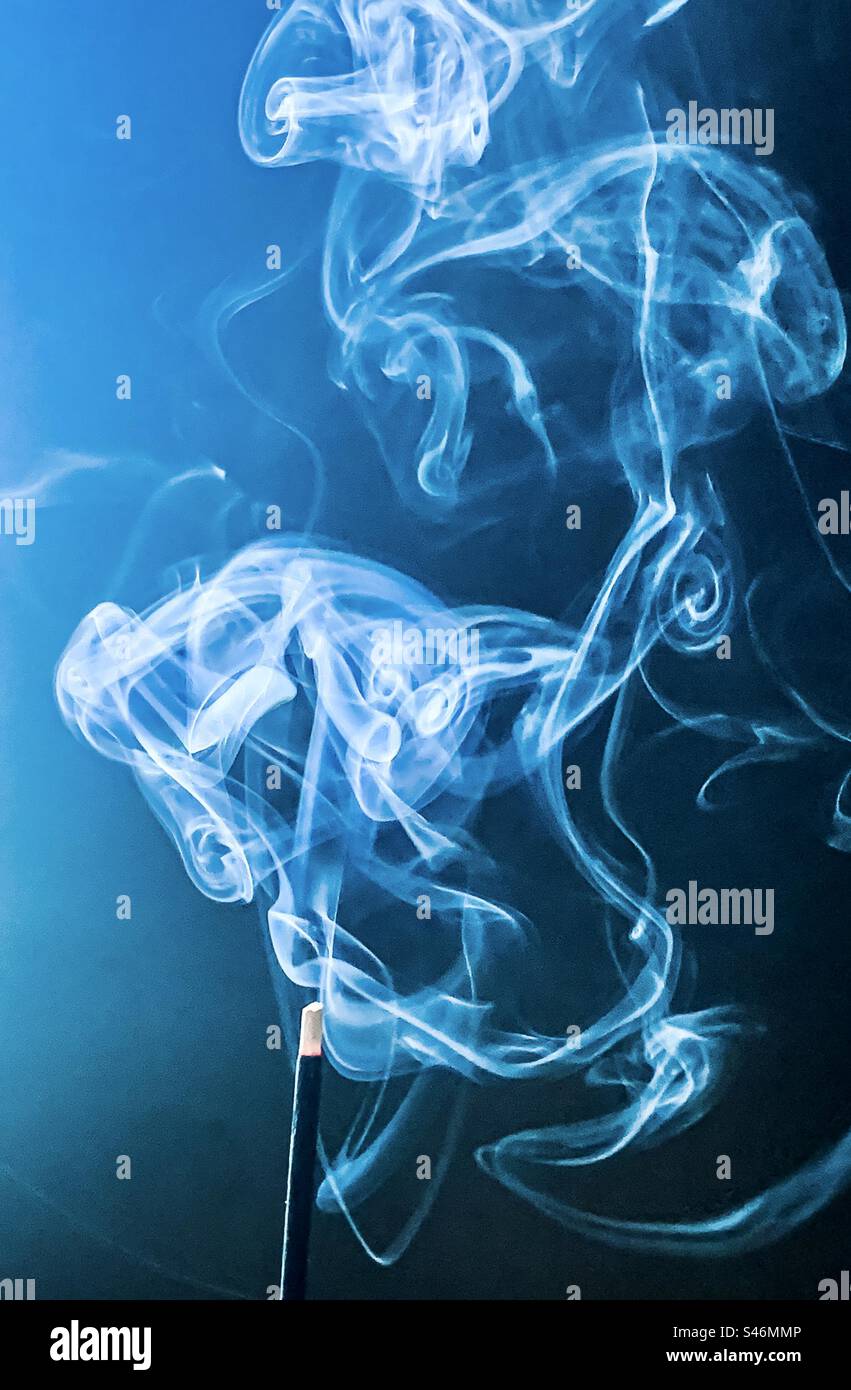 Smoke swirly from an incense stick against blue background Stock Photo