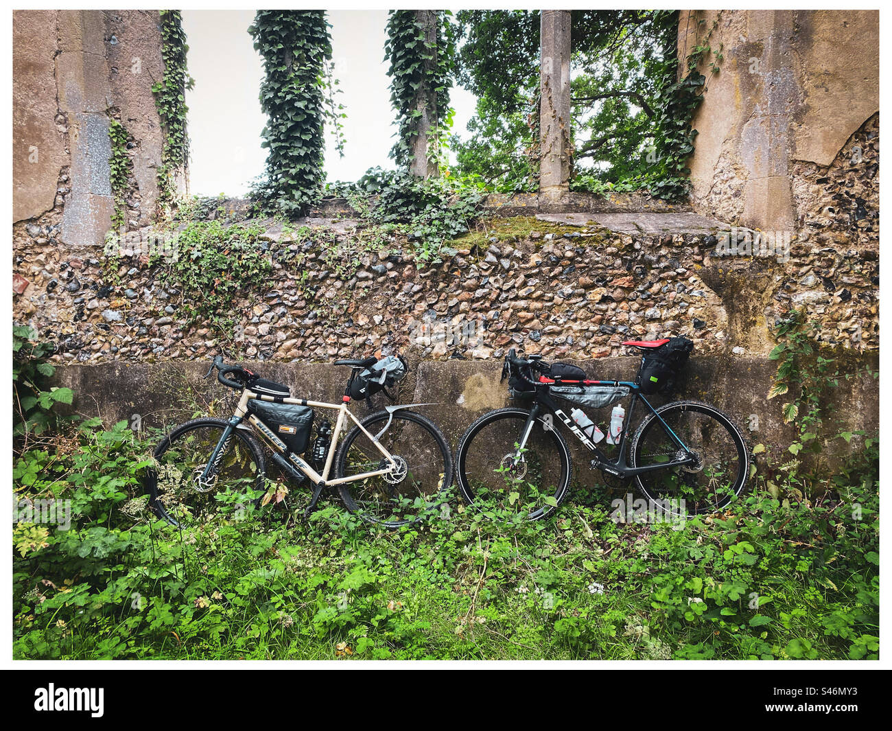 Two loaded bikes lean against the wall of an old ruined church in Norfolk England - Smartphone Captured Stock Image