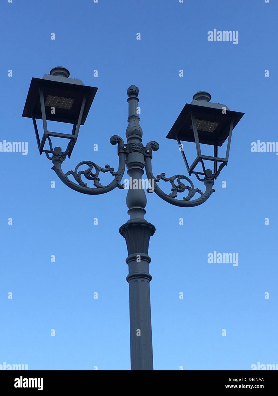 Lampione doppio nel cielo azzurro, double street lamp in a blue sky. Due lampadine, two lamps. - Smartphone Captured Stock Image