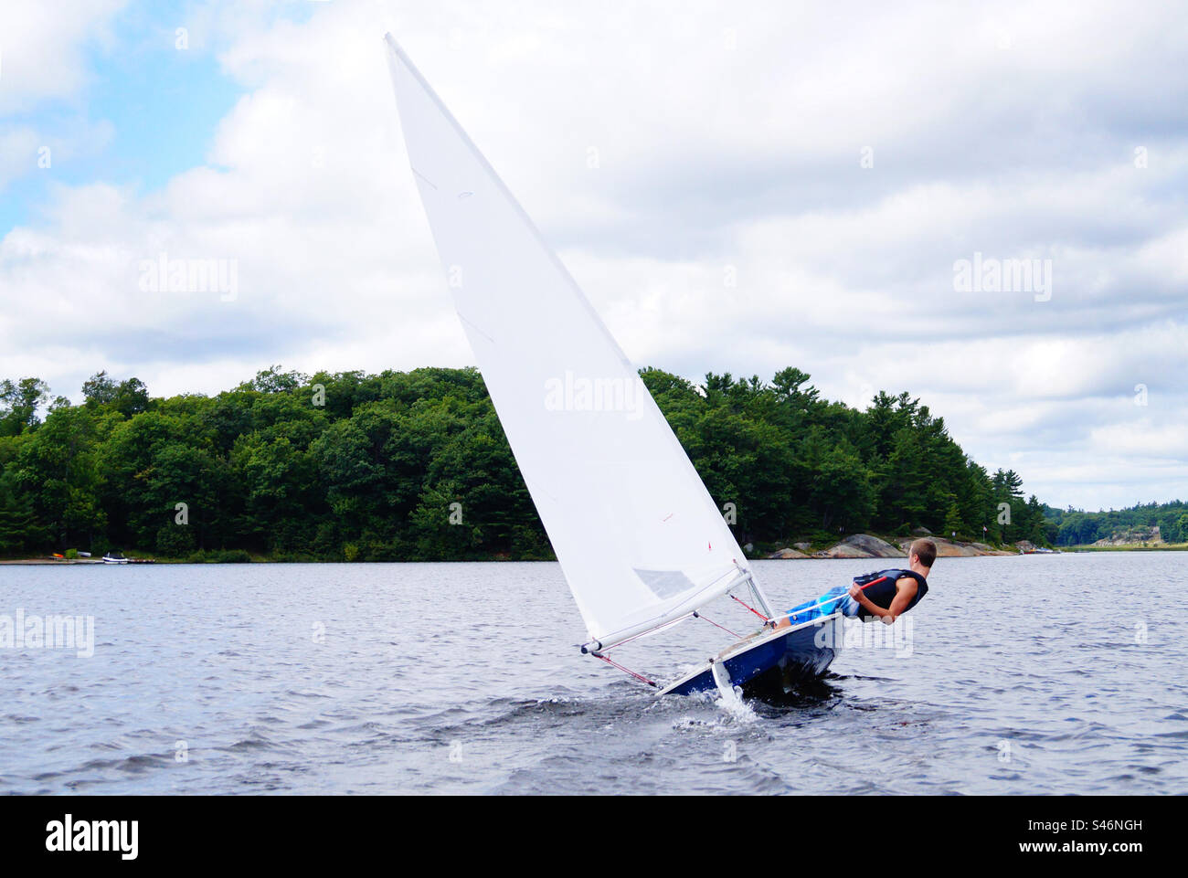 Sailing a small sailboat across a windy lake, hiking way out while boat is healing over. - Smartphone Captured Stock Image Sailing a small sailboat across a windy lake, hiking way out while boat is healing over. - Smartphone Captured Stock Image